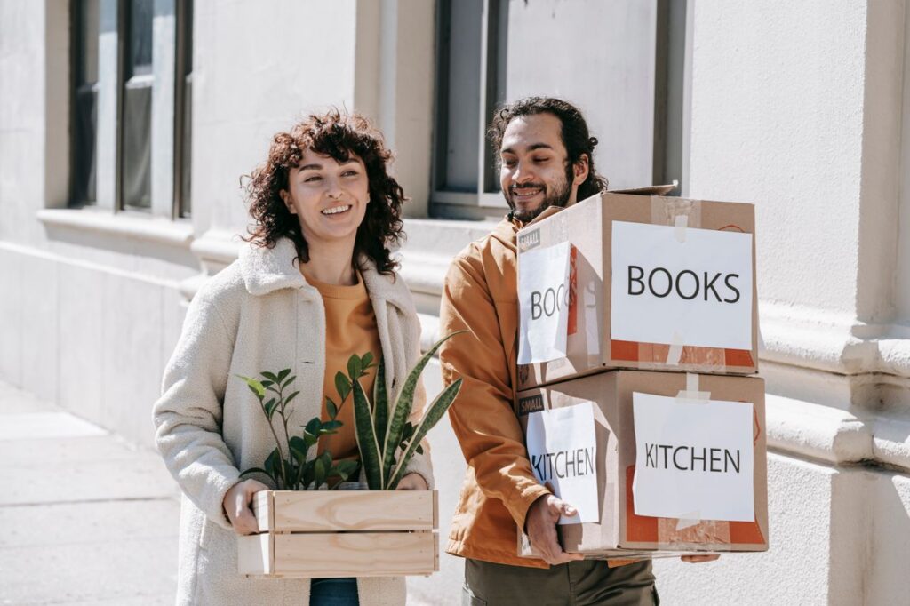 Couple carrying boxes and plants while moving into their new home