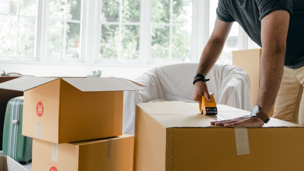 Person sealing a moving box with packing tape, part of essential moving supplies