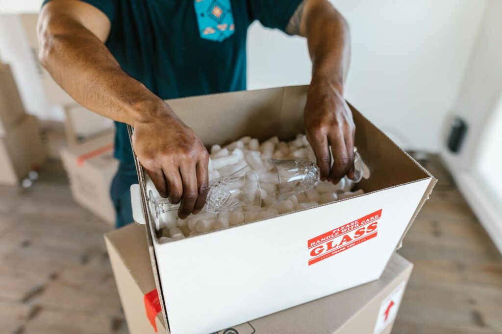 Hands carefully packing dishes and glassware into a padded cardboard box